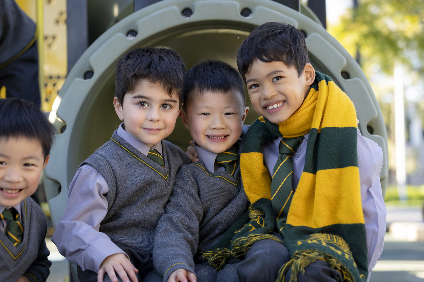 Three smiling Trinity Junior School boys together on the playground, one wearing a green and gold house scarf