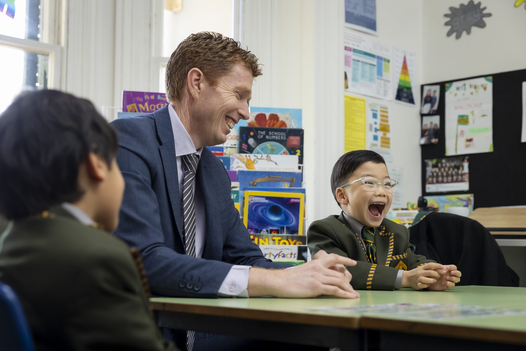 A Trinity Junior School teacher laughing with two Prep boys at their classroom desk