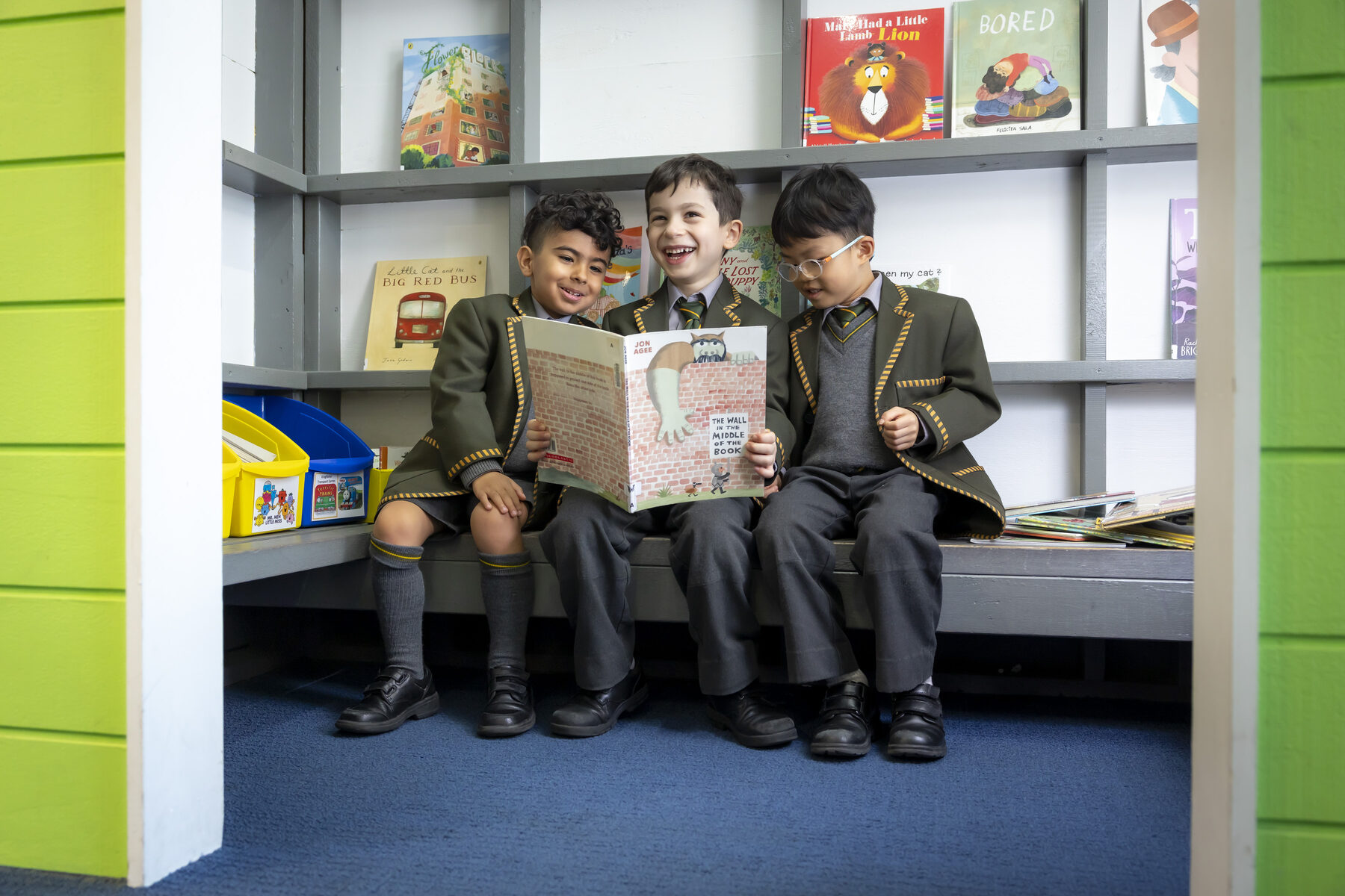 Three Prep boys laughing together while reading a picture book in the Junior School library nook
